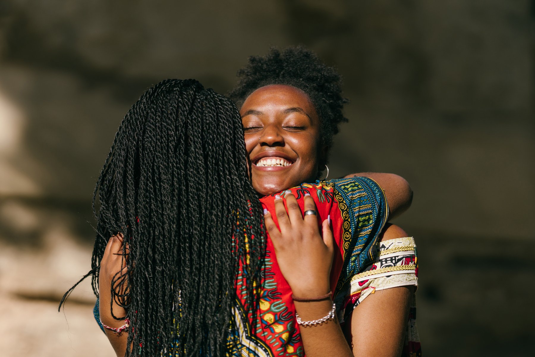 Two African Women in Multicolored Ethnic Clothes Embracing with Emotion Outdoors